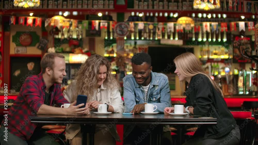 Afro-American man with friends in a cafe laughs and spends time in a cheerful company and smiling while telling stories Afro-American man with friends in a cafe laughs and spends time in a cheerful company and smiling while telling stories