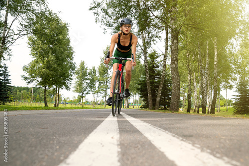 Sportswoman in uniform and helmet riding on the bike path on the background of green trees © makedonski2015