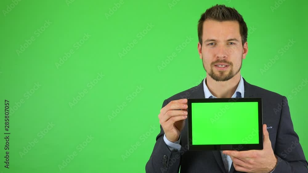 A young handsome businessman talks to the camera and holds out a tablet with green screen - green screen studio A young handsome businessman talks to the camera and holds out a tablet with green screen - green screen studio