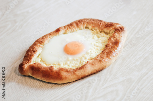 Homemade Ajarian Khachapuri with Suluguni Cheese Filled with a  Egg and Melted Butter Close Up on the white wooden background photo