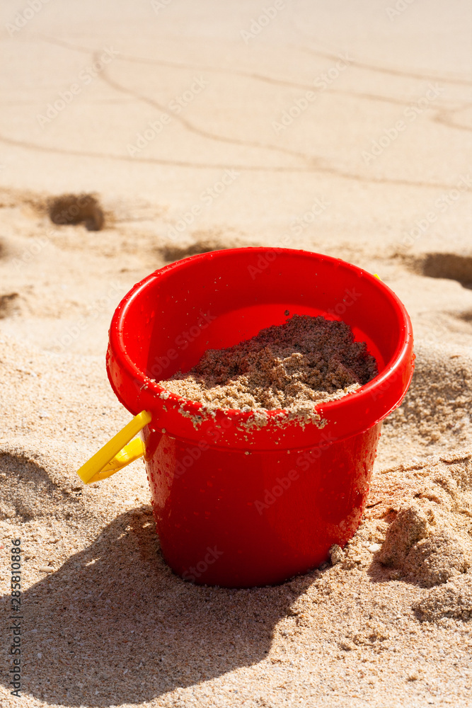 SEAU DE PLAGE EN PLASTIQUE ROUGE ET JAUNE SUR LE SABLE SEAU DE PLAGE EN PLASTIQUE ROUGE ET JAUNE SUR LE SABLE