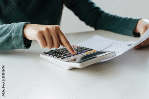 young woman using calculator for analysis and calculating family budget cost bills report on desk in home office  plan money cost saving  investment  business finance  expenses and income concept