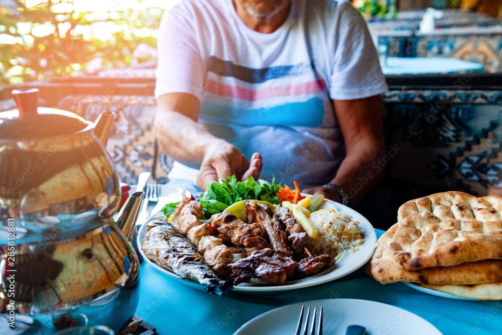 A traditional Turkish dinner is served on the street cafe table: a dish of fried fish, chicken, lamb and vegetables, bread cakes, tea. A man sits at a table