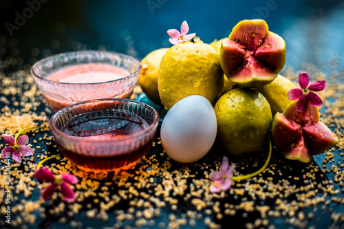 Treatment of dry skin with the help of face mask on a wooden surface consisting of honey, guava pulp, egg yolk, and some oatmeal, well mixed in a glass bowl along with raw ingredients. photo