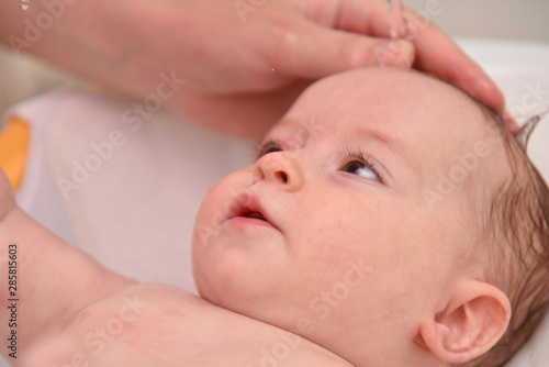 Pretty three months baby girl taking a bath by her mother at home, european child.