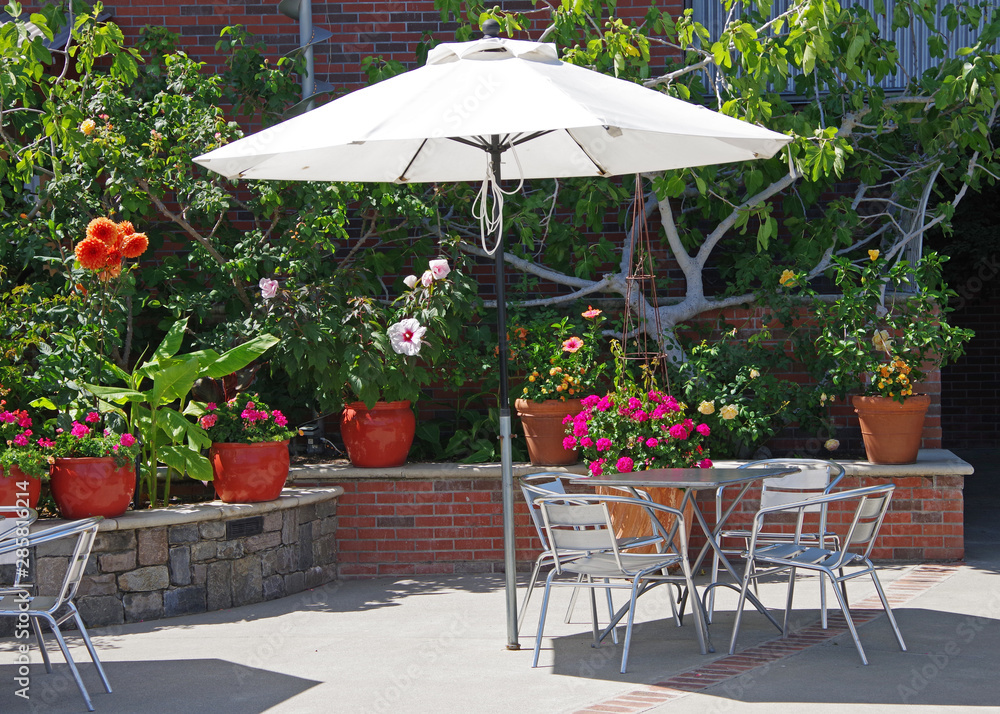 Fototapeta Coffee house style outdoor chairs and table under an umbrella in a lush garden setting on a bright summer day