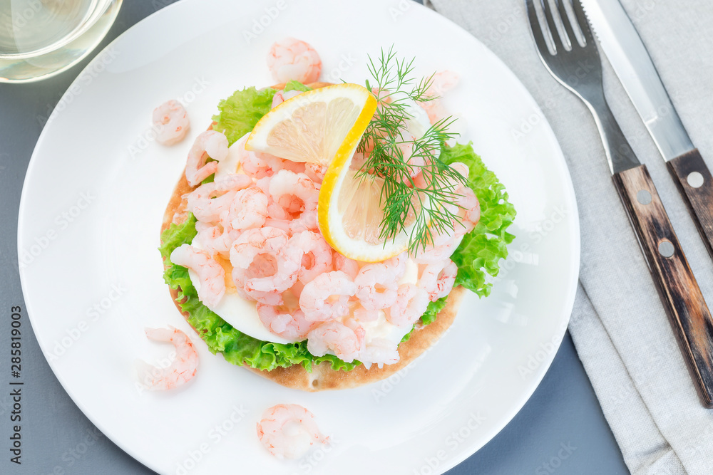 Traditional savory swedish sandwich with soft white bread vetekaka, lettuce, eggs, mayonnaise, shrimps, dill and lemon, horizontal, top view