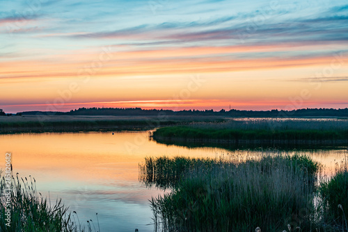 Evening sunlight on coast, pink clouds, blue sky reflection on water. Beach in summer. Seaside natural environment. Shore in Laelatu, small island in Estonia. Nature Reserve in North Europe