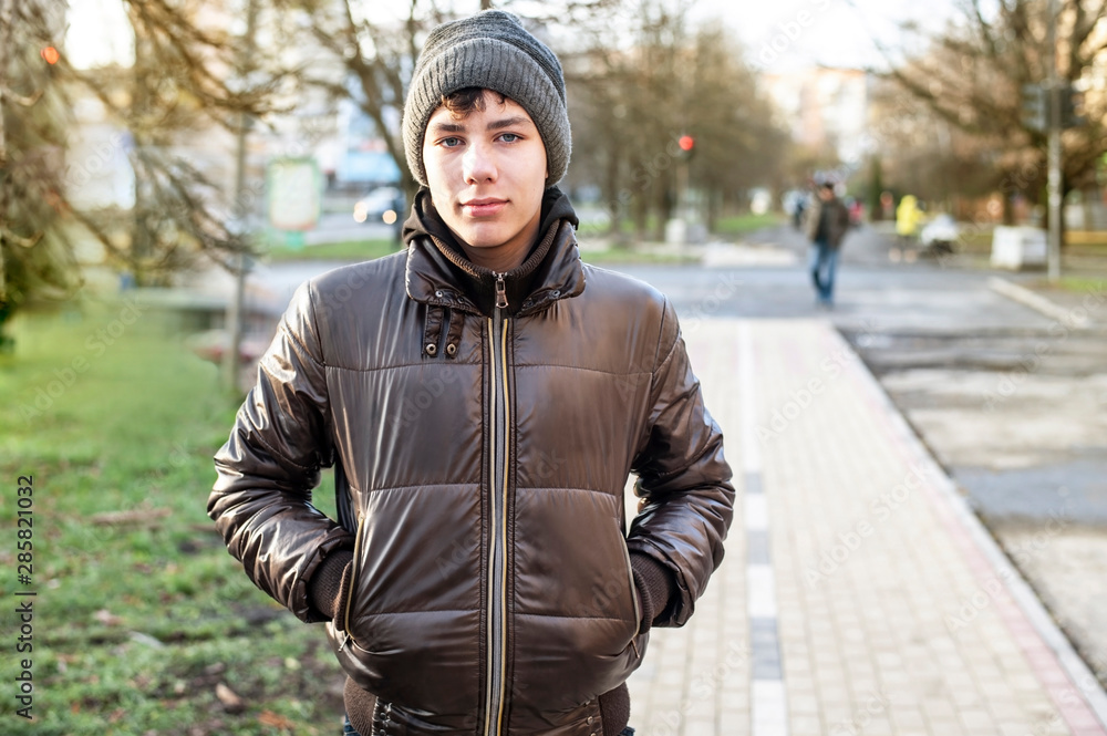 Handsome young boy, teenager in winter hat and jacket on modern city background at sunset Handsome young boy, teenager in winter hat and jacket on modern city background at sunset
