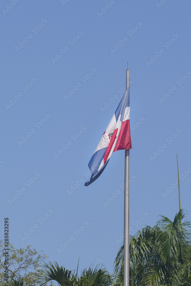 Flag of Dominican Republic (DR) waving in the wind with blue sky on background