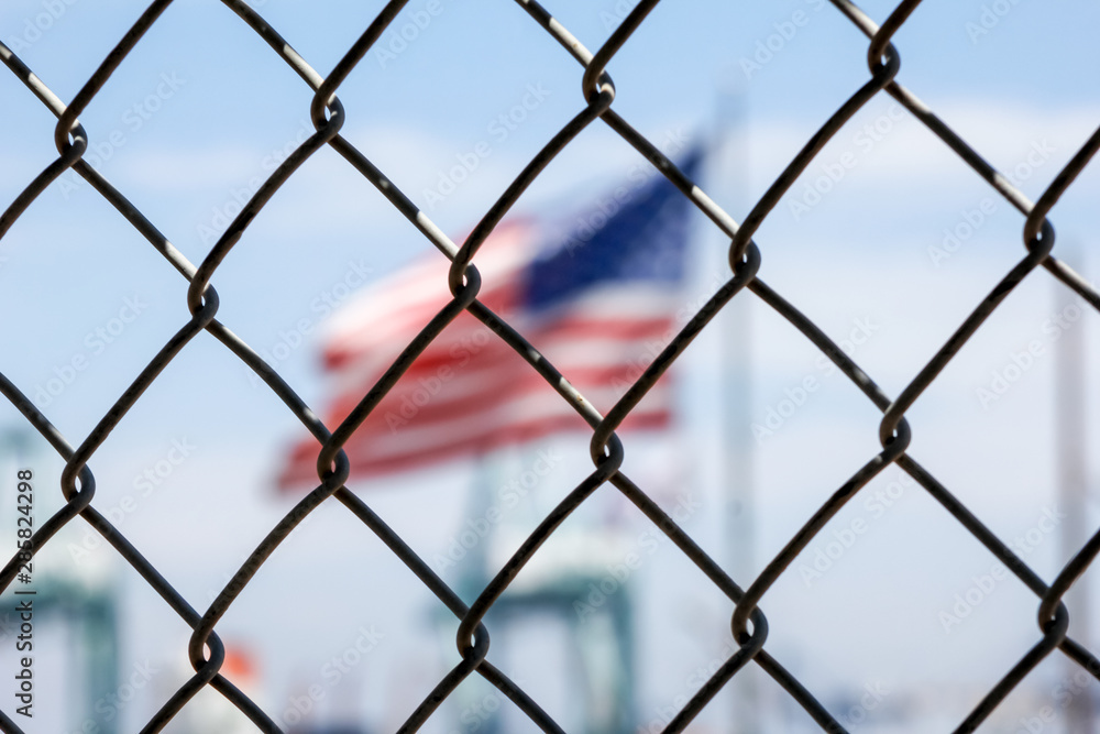 A chain link fence stands in front of a blurry United States Flag A chain link fence stands in front of a blurry United States Flag