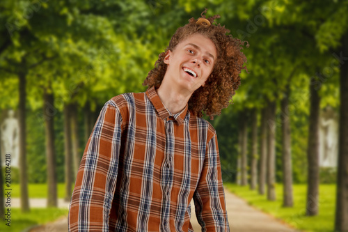 Portrait of a curly-haired young man with a wooden comb in full hair smiling in a park background. male hair care concept