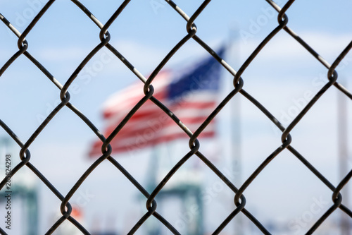 A chain link fence stands in front of a blurry United States Flag
