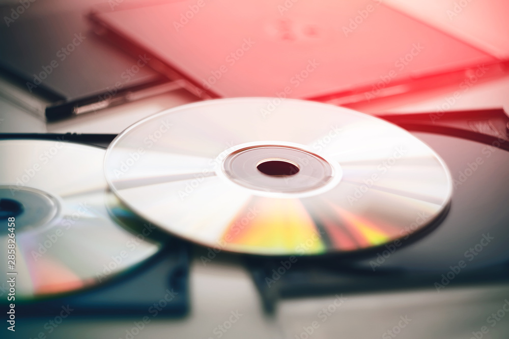 Two disks lie in black plastic packages for disks and gleam in different colors, illuminated by a bright red light. Two disks lie in black plastic packages for disks and gleam in different colors, illuminated by a bright red light.