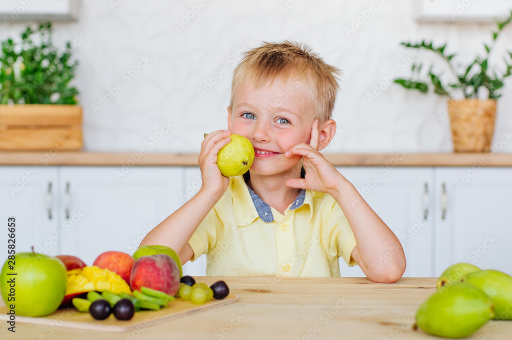 Fototapeta premium Happy little boy eating fresh pear in the kitchen