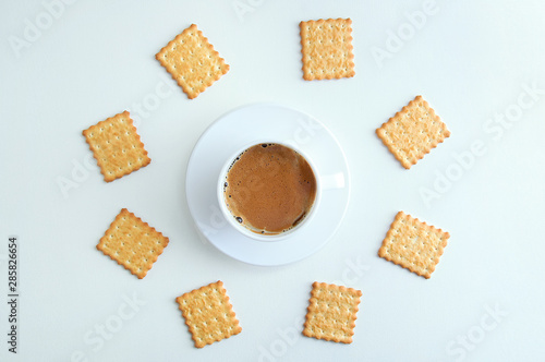 White cup and saucer with coffee foam and cracker cookies. On a white background. View from above.