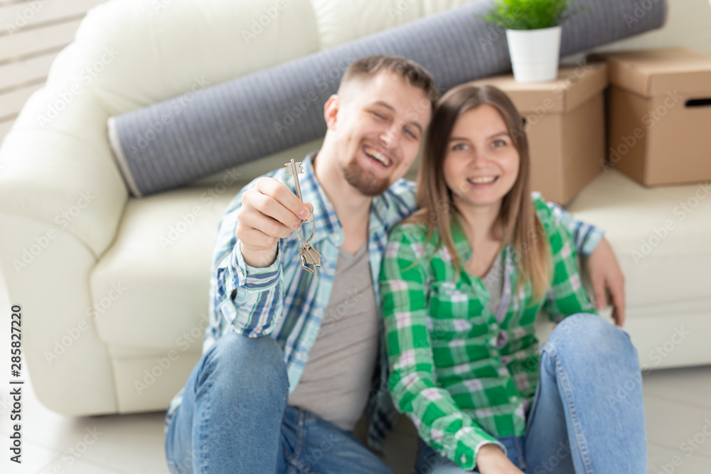 Obraz premium Young positive couple holding keys to a new apartment while standing in their living room. Housewarming and family mortgage concept.