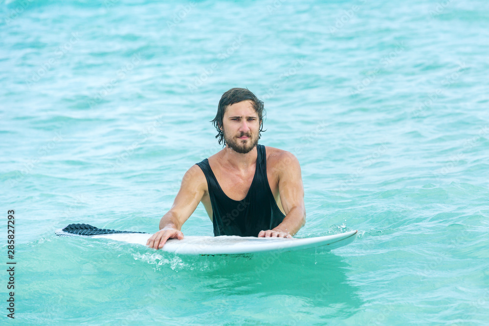 Surfer man holding a surfboard, tired coming out of the ocean