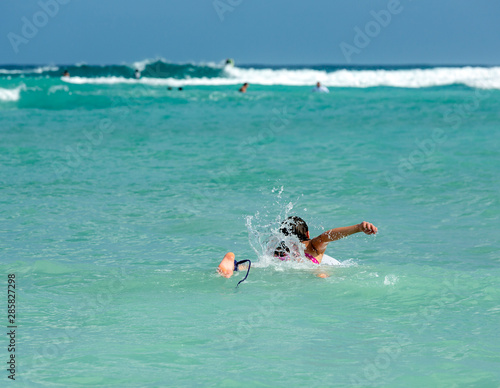 Attractive young woman on surfboard in the ocean swims to the waves