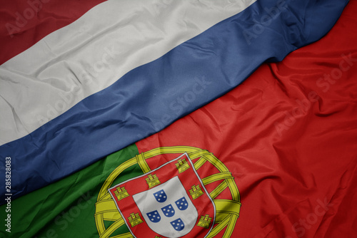 waving colorful flag of portugal and national flag of netherlands.