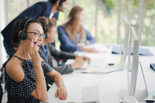 Young beautiful European operator woman with headsets working with the team in a call center.Customer support phone in headset with smiling and felling happy. Team operator call center concept.