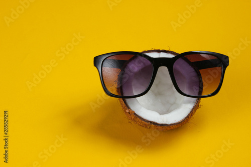 Creative fashion concept. Coconut half with sunglasses on yellow background