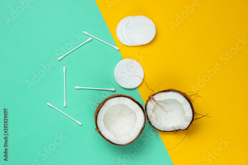 Minimalistic natural beauty concept. Coconut halves, cosmetic accessories on a blue-yellow pastel background. Top view