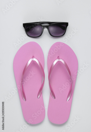 Summer still life. Beach accessories. Fashionable beach pink flip flops, sunglasses on white paper background. Flat lay. Top view