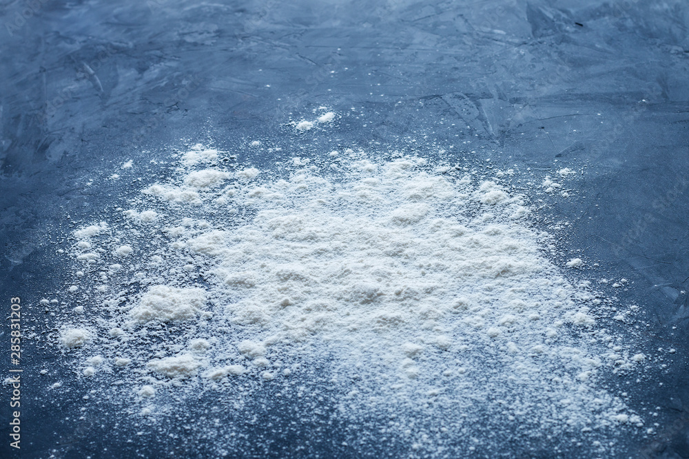 Fototapeta premium Side view of a pile of sprinkled baking white flour with shallow depth of field on a textured blue table with empty space for text