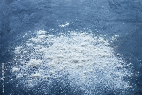 Side view of a pile of sprinkled baking white flour with shallow depth of field on a textured blue table with empty space for text