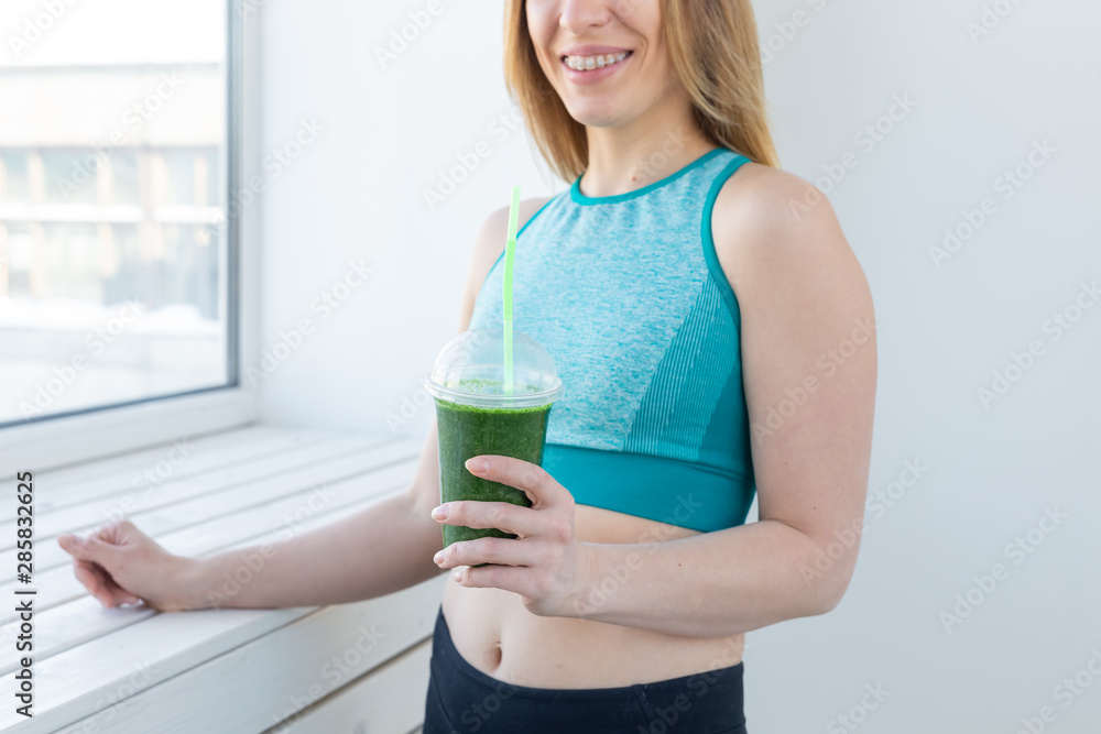 Healthy, fitness and detox concept - close up of young woman in sports wear with green smoothie smiling indoors Healthy, fitness and detox concept - close up of young woman in sports wear with green smoothie smiling indoors
