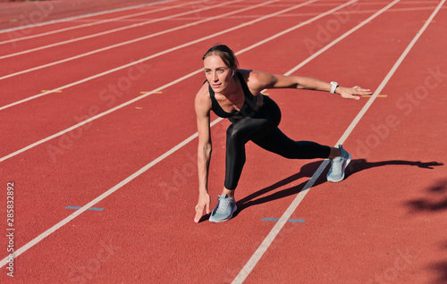 Fit woman in sportswear doing warm-up before jogging on stadium track with red coating outdoors