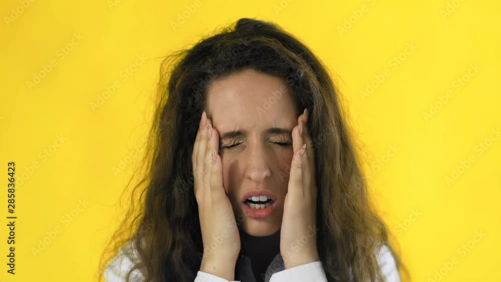 Beautiful girl is suffering from a migraine standing on a yellow background, slow motion Beautiful girl is suffering from a migraine standing on a yellow background, slow motion