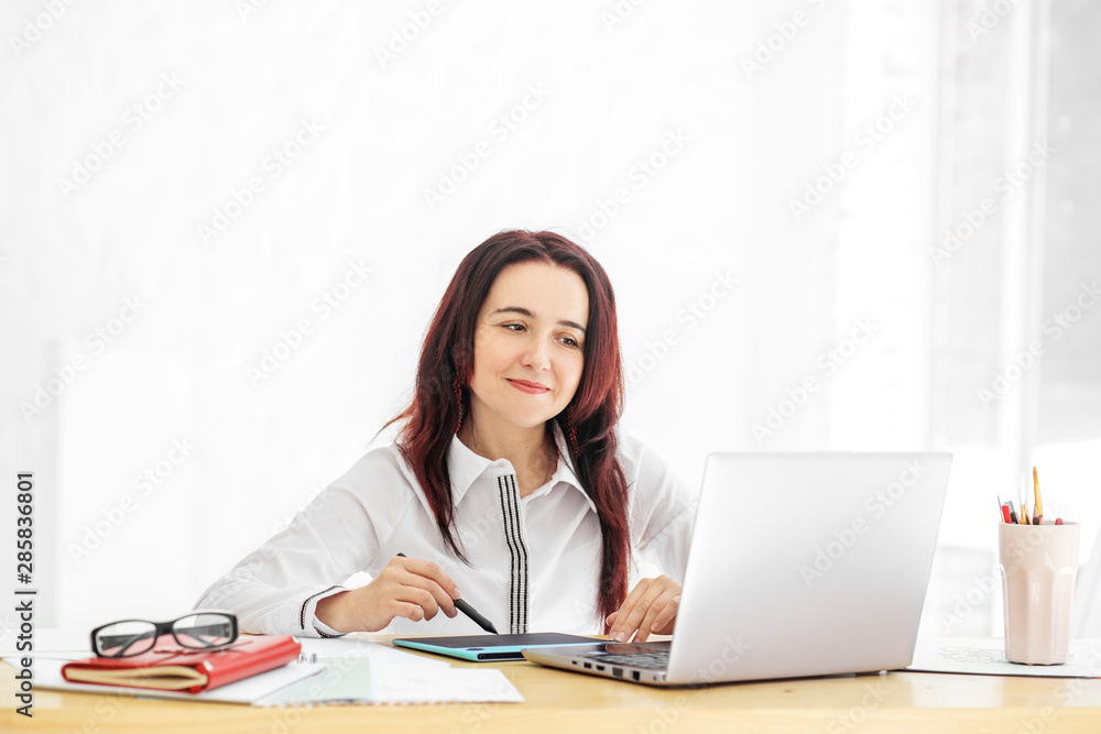 A beautiful woman is sitting at her desk and smiling. Concept for business, work, career. A beautiful woman is sitting at her desk and smiling. Concept for business, work, career.