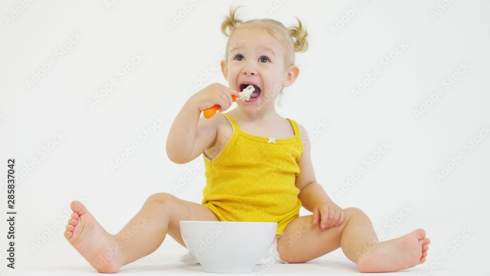 Smiling baby girl eating her breakfast on white background Smiling baby girl eating her breakfast on white background