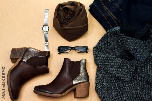 Set of women's autumn, winter clothes: blue jean, coat, brown boots and eyeglasses and brown scarf, hand watch. Fashionable clothes for walks, flat lay