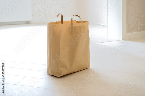 A brown paper bag is on the floor of the new apartment. Close up.