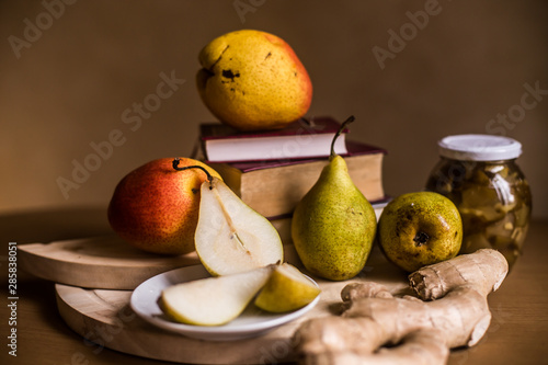 The photo shows fresh pears, a jar of jam and ginger root on the background of the tablecloth.