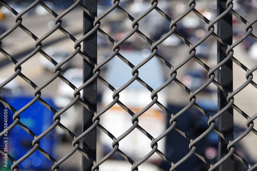 Close-up sectional view focused on the fence of a bridge railing with freeway traffic below Close-up sectional view focused on the fence of a bridge railing with freeway traffic below