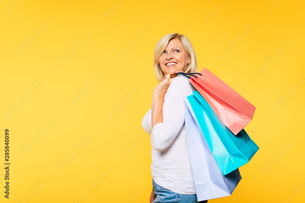 Buyer. Consumer. Sale. Customer. Online Shopping. Happy laughing blonde senior woman with colorful paper shopping bags is posing and has a fun after good visit of mall. Banner photo Buyer. Consumer. Sale. Customer. Online Shopping. Happy laughing blonde senior woman with colorful paper shopping bags is posing and has a fun after good visit of mall. Banner photo