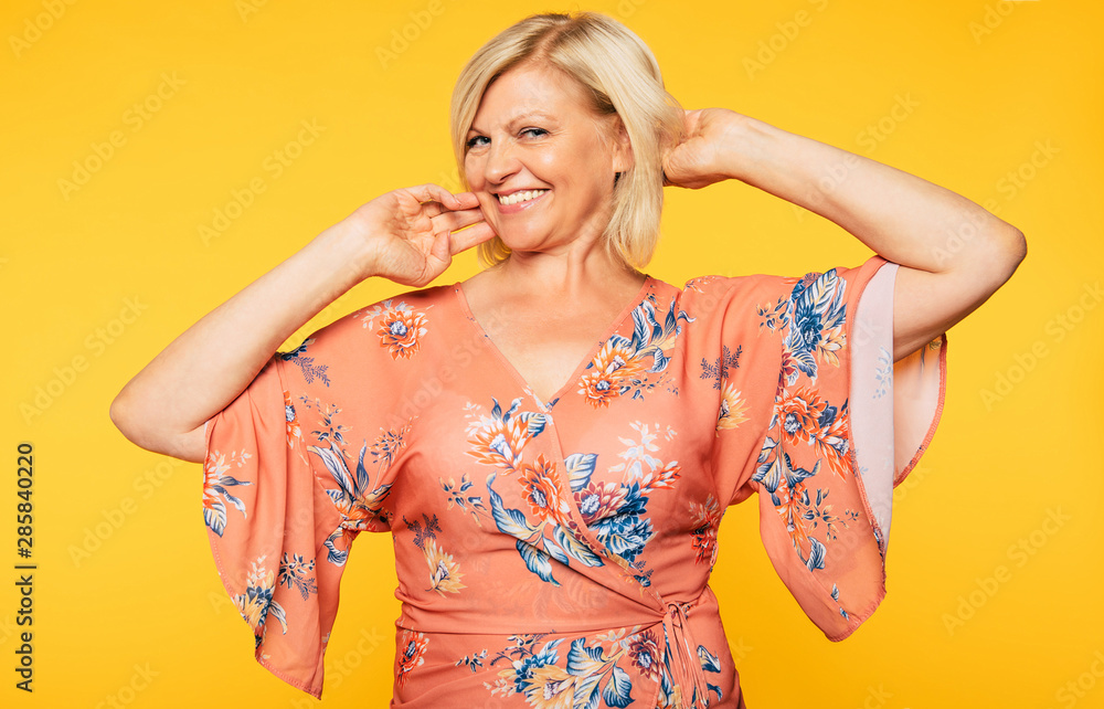 Beautiful smiling and happy cute senior woman in colorful clothes is posing on yellow background. Holidays and vacation. Summer mood