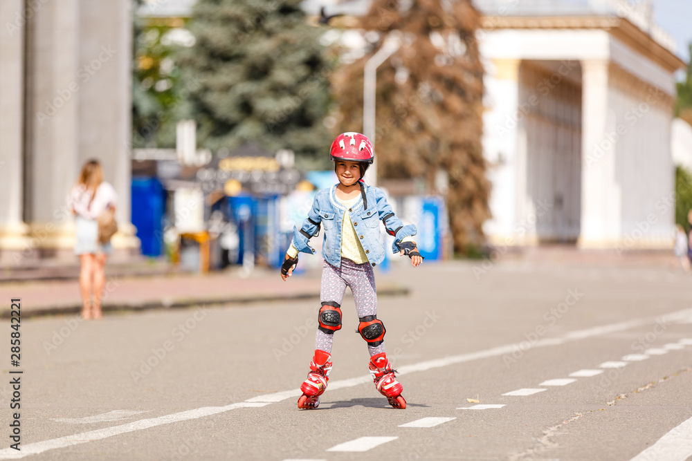 Funny Little pretty girl on roller skates in helmet riding in a park. Healthy lifestyle concept.