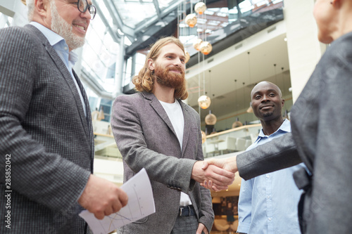 Low angle portrait of group of business people shaking hands with handsome bearded man standing in office hall after successful partnership meeting, copy space