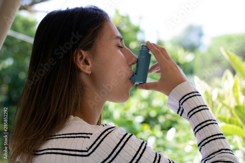 Health and medicine - Young girl using blue asthma inhaler to prevent an asthma attack.