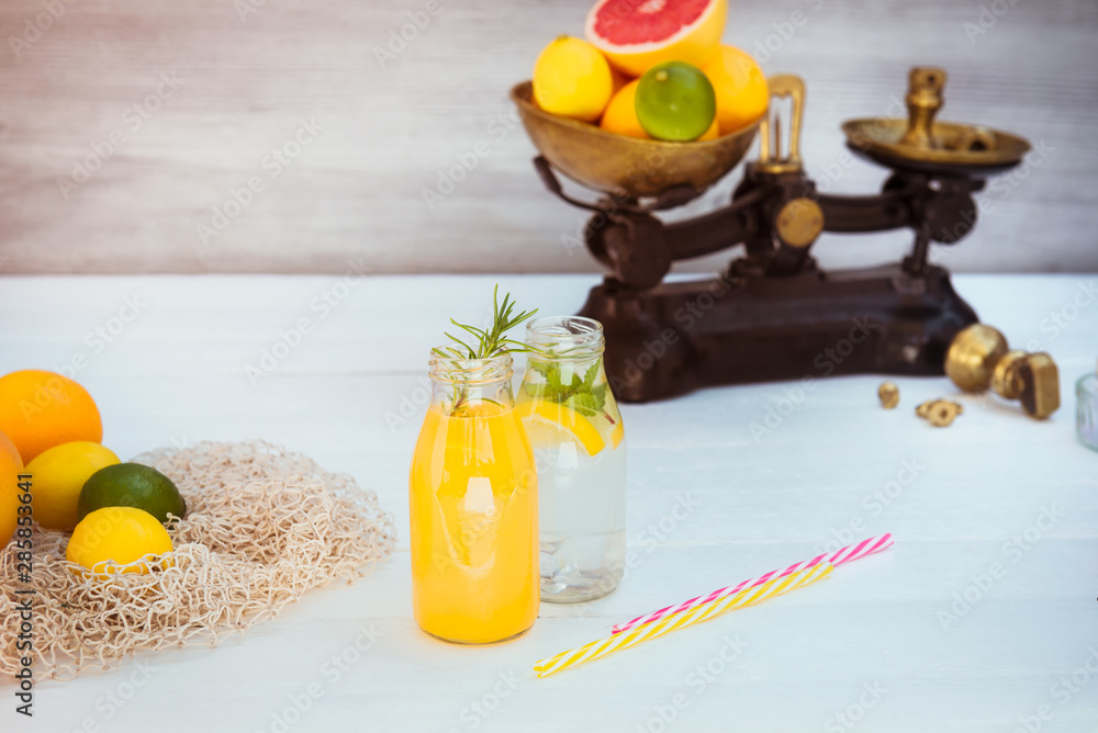 Φωτογραφία Two bottles with homemade lemonade and orange fresh juice with mint and ice on the white wooden background with fresh citrus in vintage scale and some friuts around
