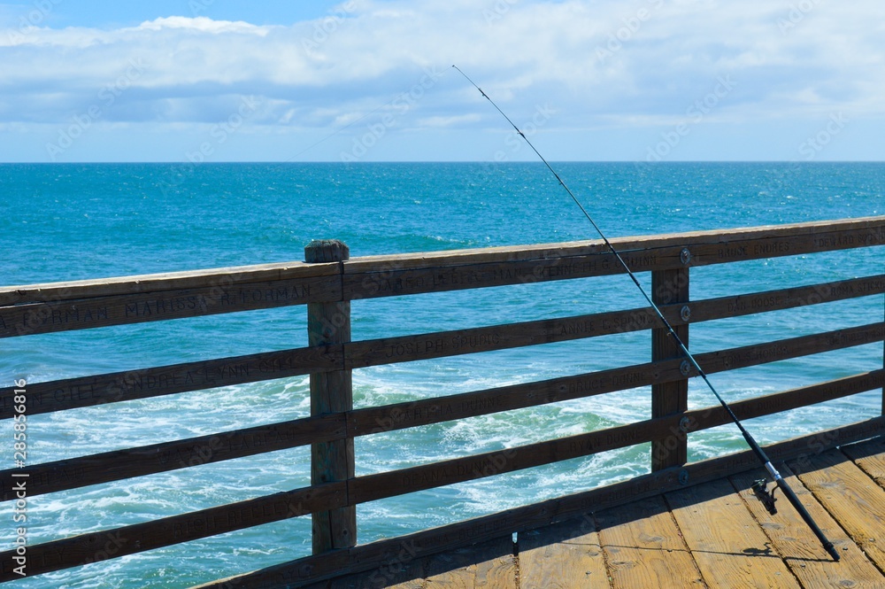 Fishing pole extends over the ocean off a wooden pier Fishing pole extends over the ocean off a wooden pier