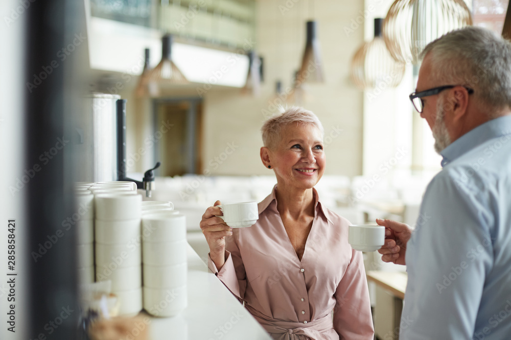 Obraz premium Portrait of two smiling senior business people , man and woman, chatting cheerfully at coffee break in office, copy space
