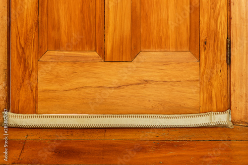 A light coloured draught stopper sits on the floor at the base of a wooden door photo