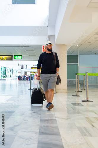 Young man walking through an airport terminal carrying a suitcase