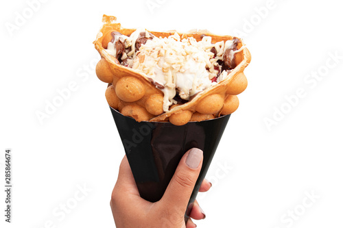 A girl holds isolated bubble waffle with white chocolate particles. photo